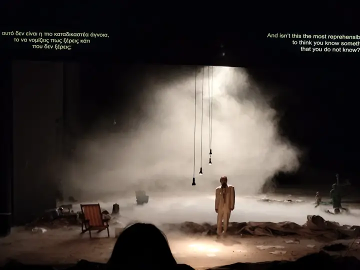 Titles projected on the set, Greek on one side and English on the other.